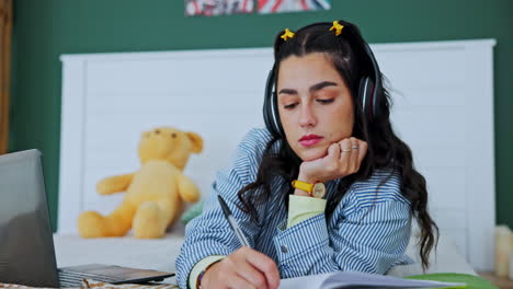 woman studying with laptop and headphones in bedroom