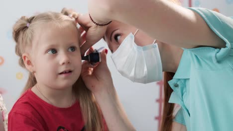 a pediatrician in a hospital checks the ear of a little girl.