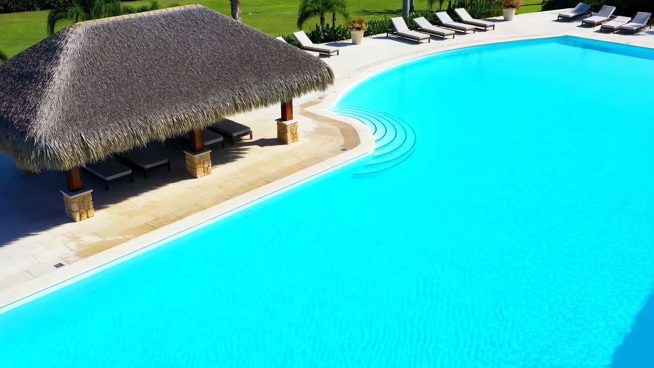 Luksus resort pool med palapa, solbeskinnet turkis vand, buede trin, skyggefuld stråtækt cabana, række af liggestole.