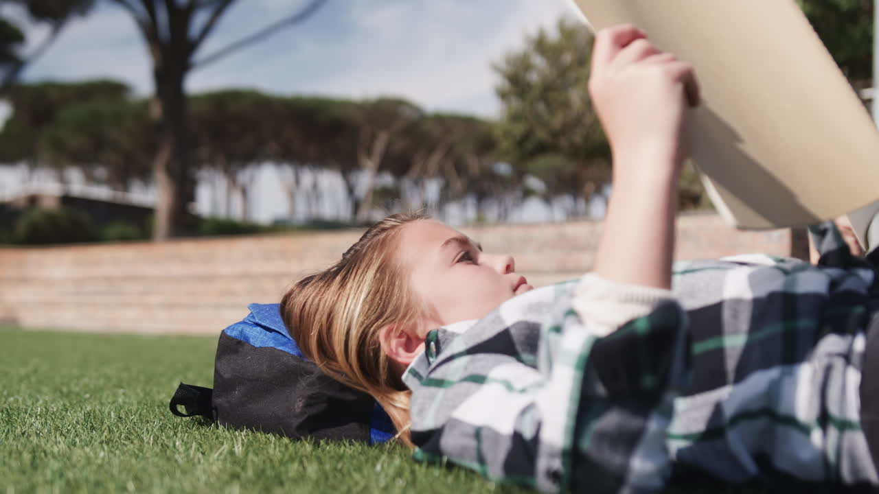 Young girl relaxing on grass reading book outdoors, enjoying sunny day, at school