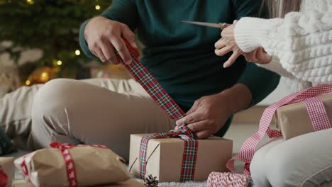 hands of unrecognizable couple packing christmas present together at home.