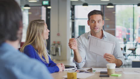 business team having meeting sitting around table discussing document in modern open plan office