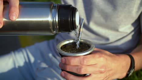 man pouring hot water into yerba mate drink from vacuum flask