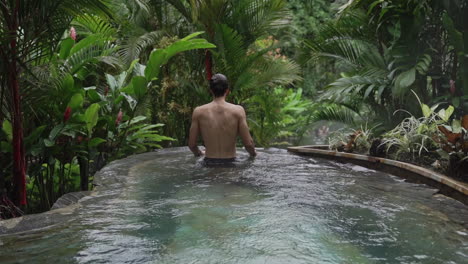 man in lavish infinity pool in rain forest looking out at surroundings