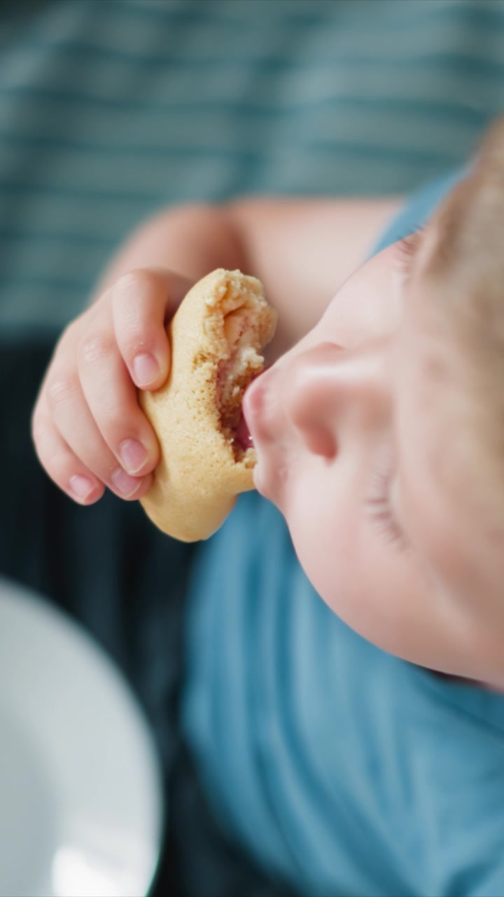 Close up of young boy eating food holding and taking bites from snack with visible hand movements. scene includes details like his striped shirt soft lighting indoor setting possibly at home