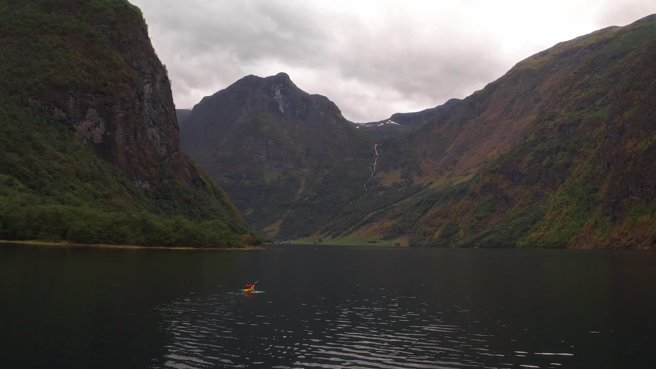 Solitary kayaker paddling in a serene Norwegian fjord surrounded by mountains