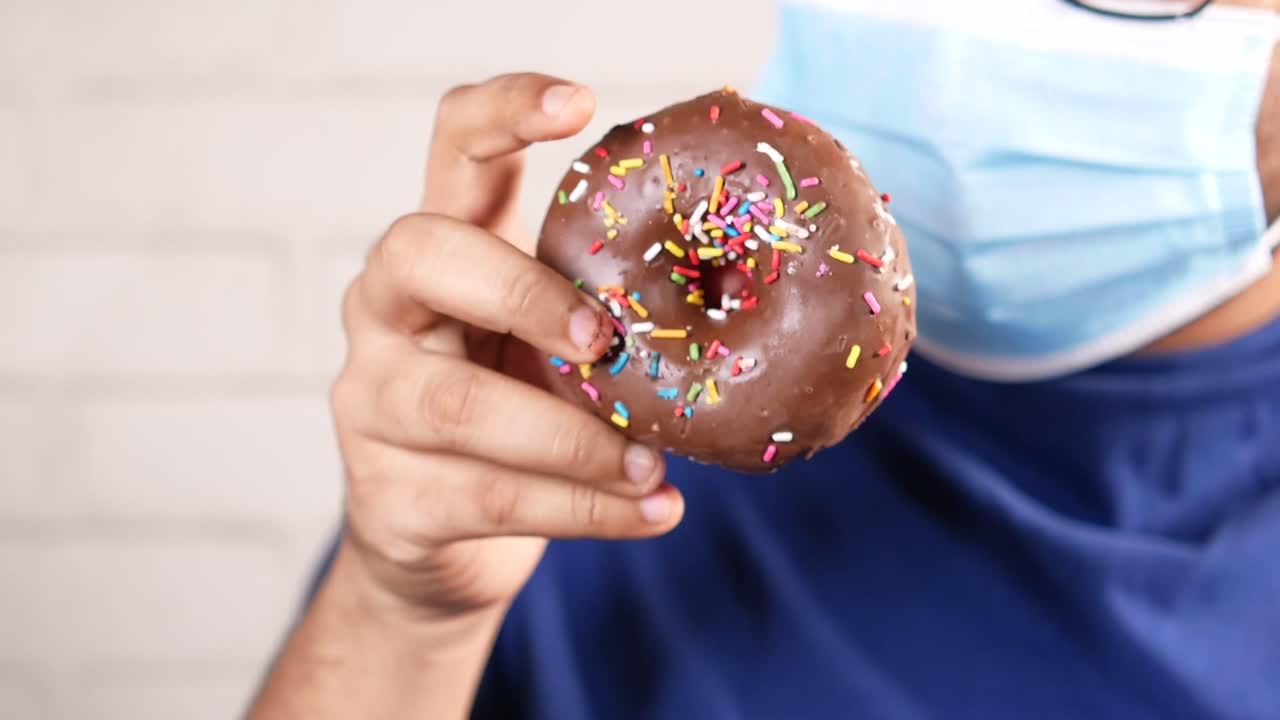 persona comiendo una rosquilla de chocolate con una máscara