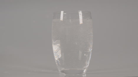 ice cubes falling into glass with sparkling water against a white studio background