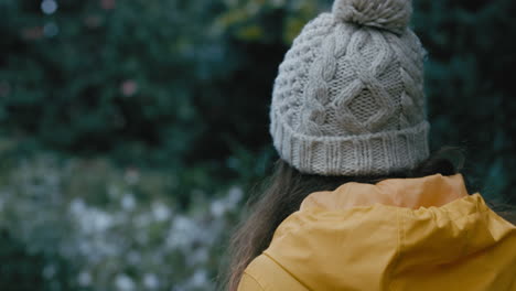 achteraanzicht jonge vrouw die in het park loopt met een gele jas en geniet van de natuur op een bewolkte dag