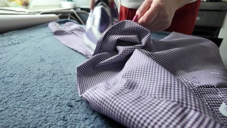 an elderly woman irons a shirt for her husband