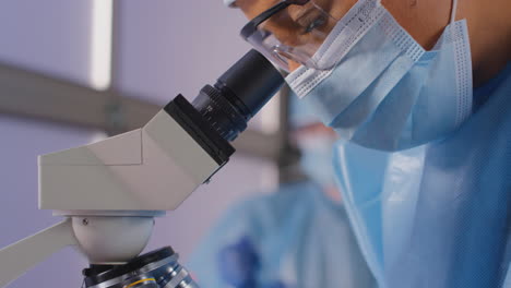 female lab worker wearing ppe analysing samples with microscope holding test tube labelled omicron