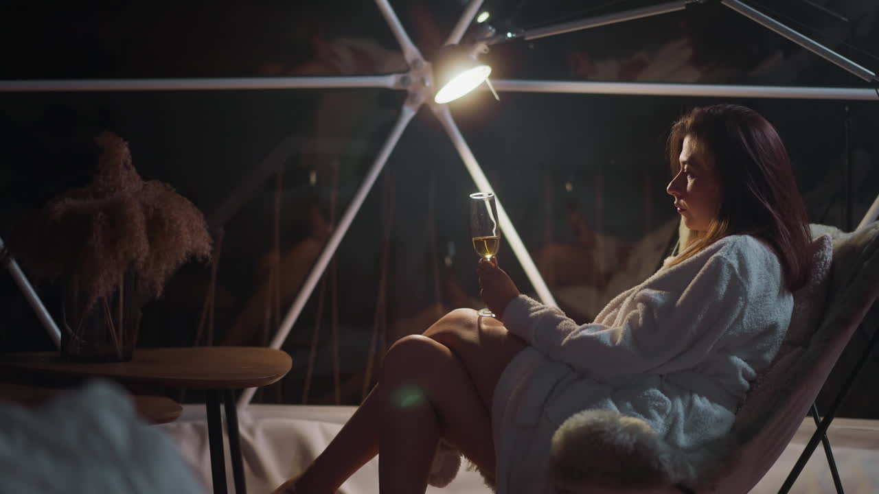 la mujer saborea la soledad por la noche disfrutando del suave resplandor de la luz de la linterna en compañía de sus propios pensamientos errantes. la mano delicada sostiene el vaso sin esfuerzo.