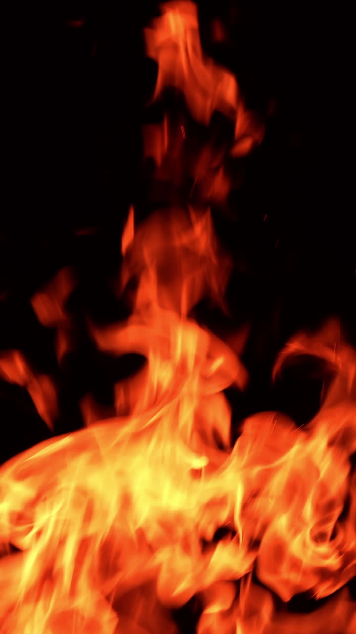 Tongues of flame licking the darkness. Tiny orange spots of fire fly around in the air. Vertical video