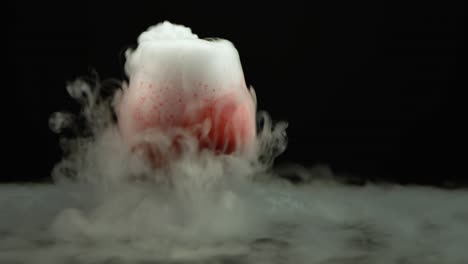 red blood drink in wine glass with the effect of dry ice - red blood drink in cognac glass with the effect of dry ice on black background at studio, chemical reaction with smoke on dark surface
