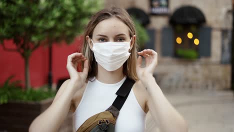 Mujer-Poniéndose-Una-Máscara-Médica-Para-Protegerse-Del-Coronavirus-Al-Aire-Libre,-Vista-Frontal