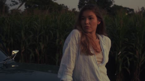 Woman Leaning on Vintage Car in Cornfield at Sunset