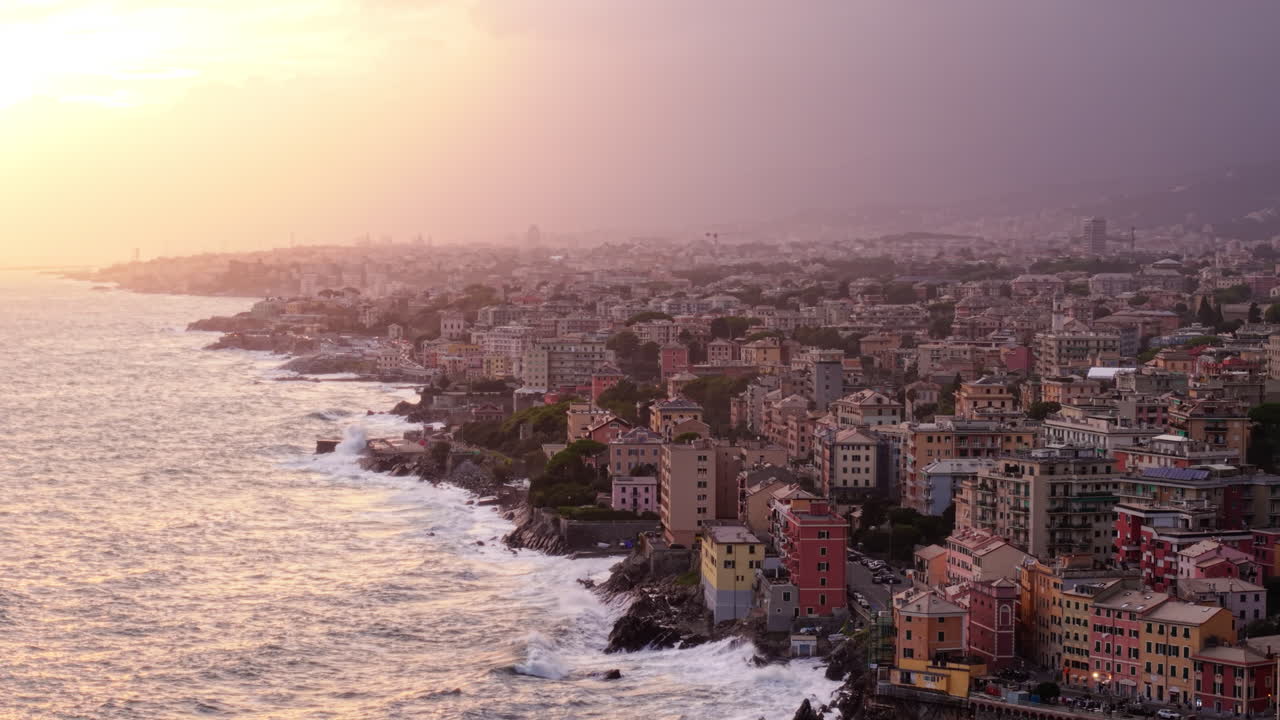 Vista aerea con drone di case costiere e onde che si infrangono a Genova, Italia, al tramonto
