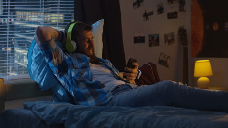 man relaxing in bed with headphones and phone