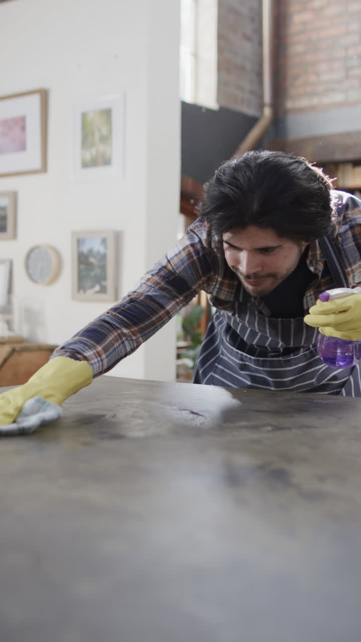 Vertical video of biracial man cleaning worktop in kitchen, slow motion