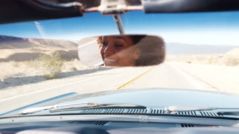 mujer joven conduciendo un coche abierto, visto en el espejo retrovisor