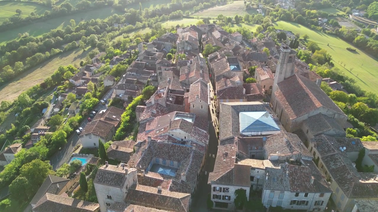 Fransa kırsalında, Cordes Sur Ciel'de, yeşil tarlalarla çevrili bir dağ tepesindeki küçük eski ortaçağ tuğla kasabasının güneşli bir günde drone ile havadan çekilmiş kuşbakışı görüntüsü.