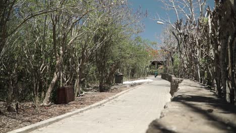 Side-wide-shot-of-couple-tourists-walking-in-Balinese-park,-bodies-covered-from-the-sun