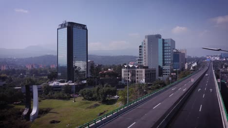 Aufnahme-Der-Aufgeständerten-Vierspurigen-Randstraße-Im-Süden-Von-Mexiko-City,-Im-Hintergrund-Sieht-Man-Einige-Firmengebäude-Oder-Hotels,-Der-Tag-Sieht-Leicht-Bewölkt-Und-Sonnig-Aus