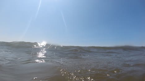 Cámara-Lenta-De-Las-Olas-Del-Mar-Rompiendo-Y-Engullendo-La-Cámara-Con-Burbujas-Y-Sol-Caliente-En-El-Cielo-Azul