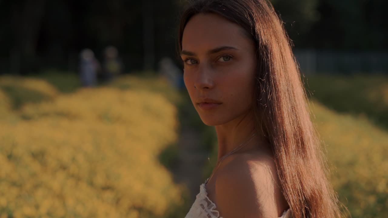 Ung kvinde med langt hår ser ind i kameraet på en gul blomstermark.