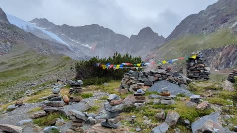 wide view of worn out nepalese prayer flags in the wind in front of stones and bushes and remote glacier