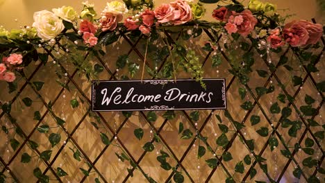 Welcome-drinks-sign-hanging-on-a-multicolour-decorated-wooden-fence-with-ace-shape-and-flowers-around-for-a-wedding