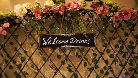 welcome drinks sign hanging on a multicolour decorated wooden fence with ace shape and flowers around for a wedding