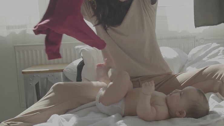 Mamma felice che sveste il suo bambino carino a casa
