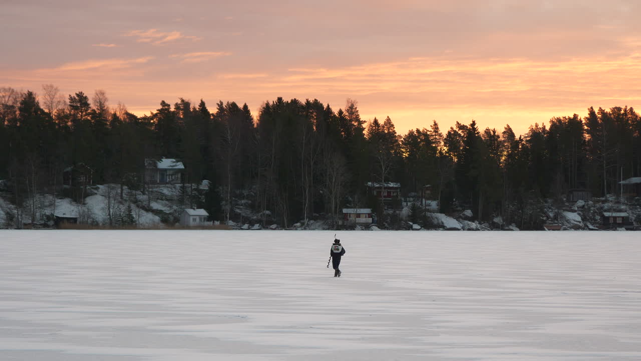 Fisherman walking on frozen lake searching for the perfect spot for ice fishing, golden morning sky