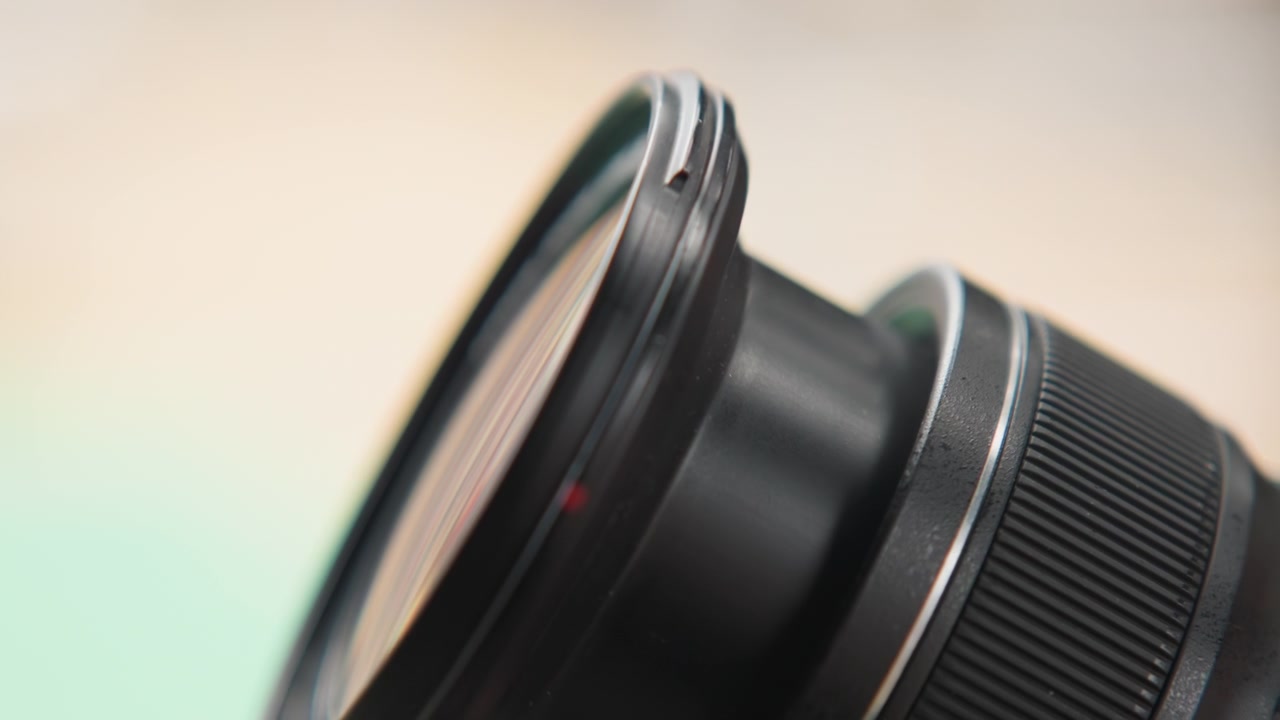 Primo piano di un obiettivo fotografico con graffio, scena di riparazione in studio che mostra una mano che tiene l'elemento frontale, vista dettagliata del bordo e del vetro, sfondo bokeh soffuso, atmosfera tecnica tesa, ispezione attenta.