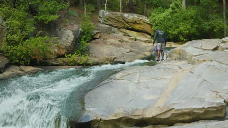 A-man-searches-for-something-on-a-giant-rock-as-a-fast-moving-stream-passes-by