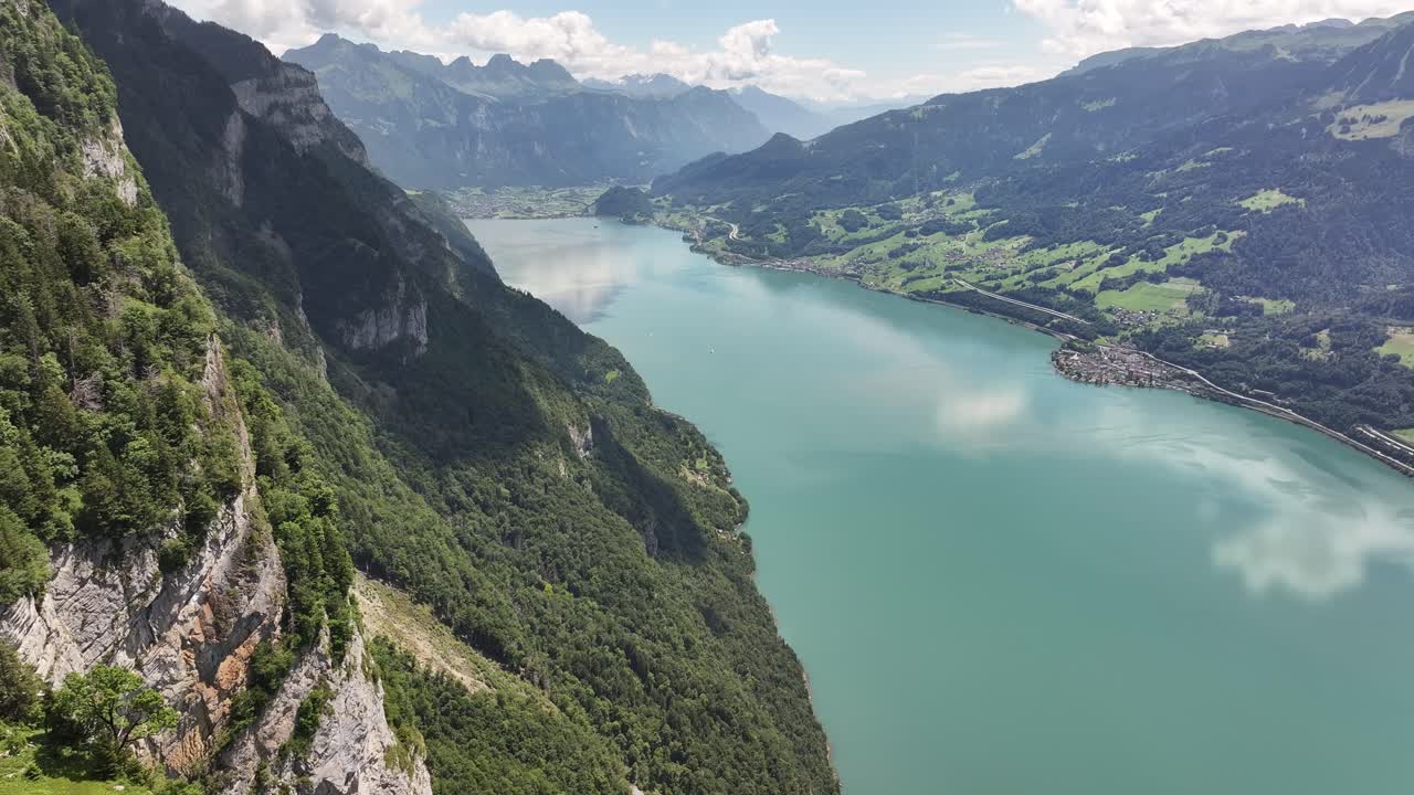 Drone aerial view of turquoise Walensee, steep alpine cliffs and lush Swiss valleys on bright summer day