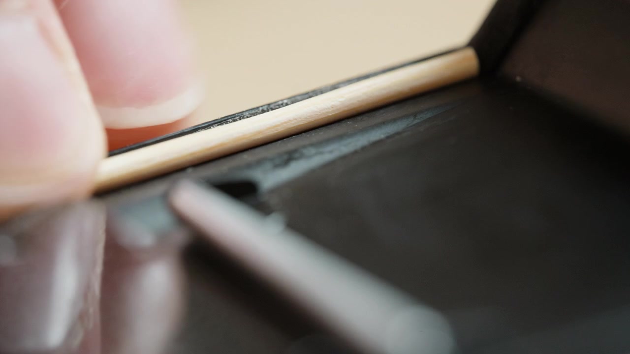 Close-up of fresh self-adhesive light seals in a vintage 35mm camera, pressed firmly into the film channel with a small wooden stick. The finishing step of analog restoration – seating the seals light