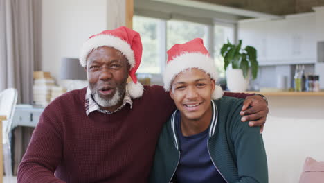 Happy-african-american-father-and-son-in-christmas-hats-having-video-call-and-embracing,-slow-motion