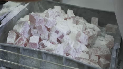 a factory worker removes the finished squares of turkish delight from a conveyor belt and places them on a tray