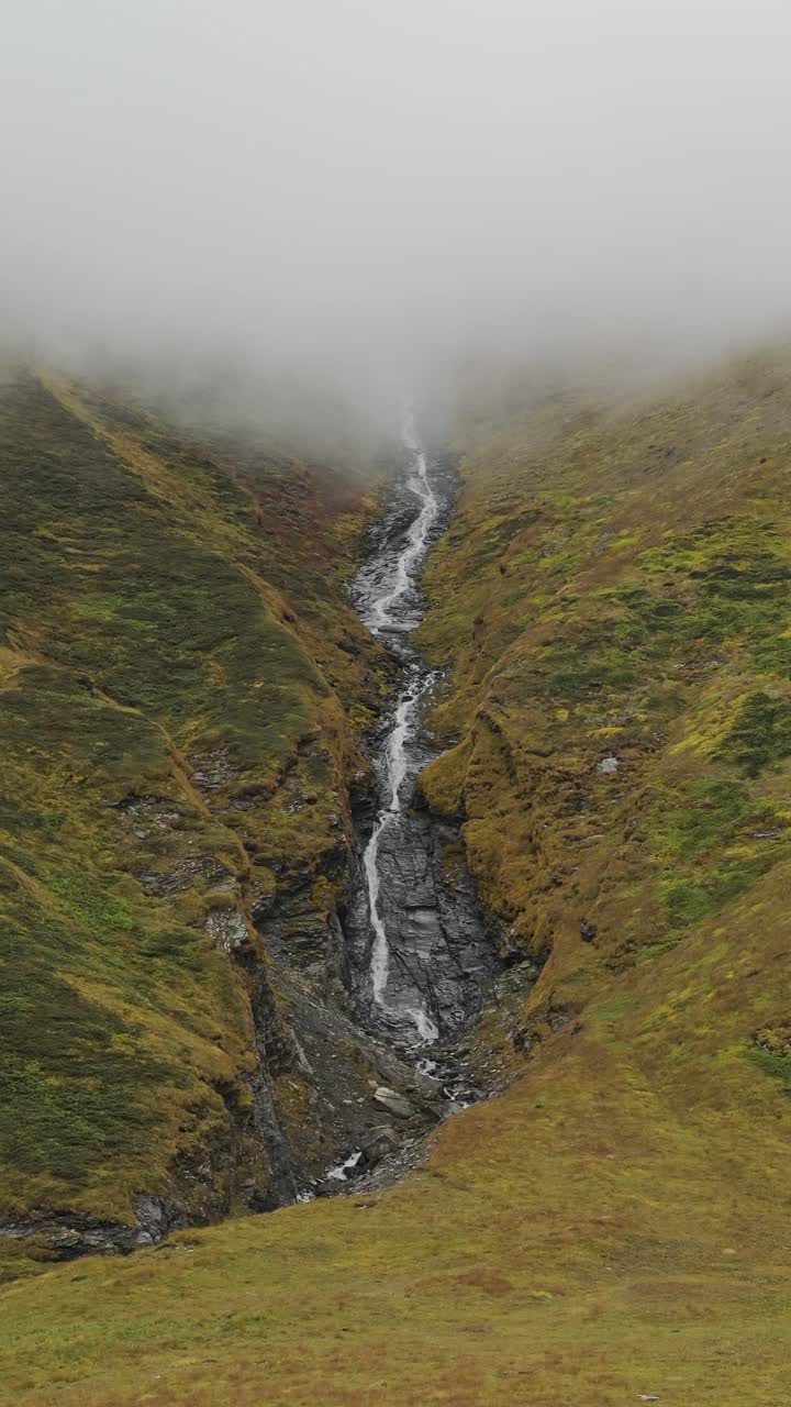 cataratas de alta altitud en las montañas de nepal, video vertical para redes sociales instagram reels y tiktok de un arroyo y río que desciende por las montañas del himalaya en paisajes de nubes de mal humor