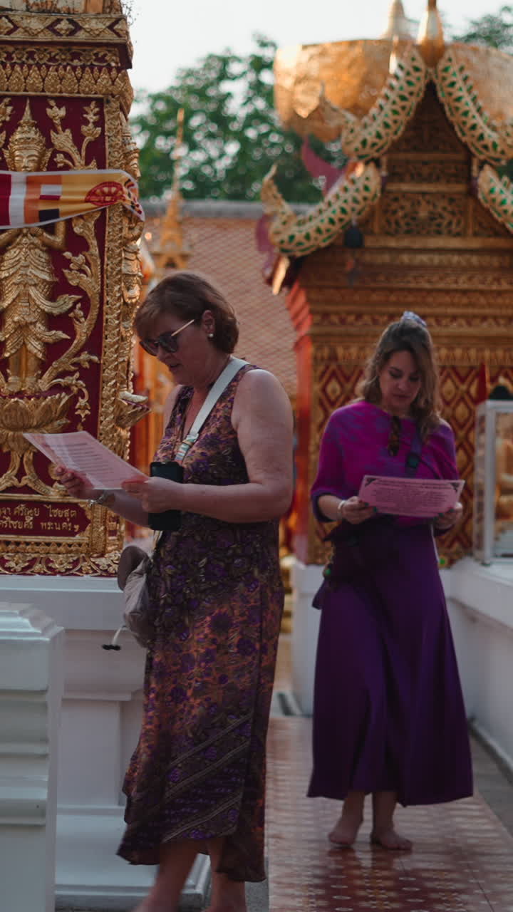 Dua Wanita Turis Berjalan Tanpa Alas Kaki dan Membaca di Kuil Thailand Berwarna Emas.