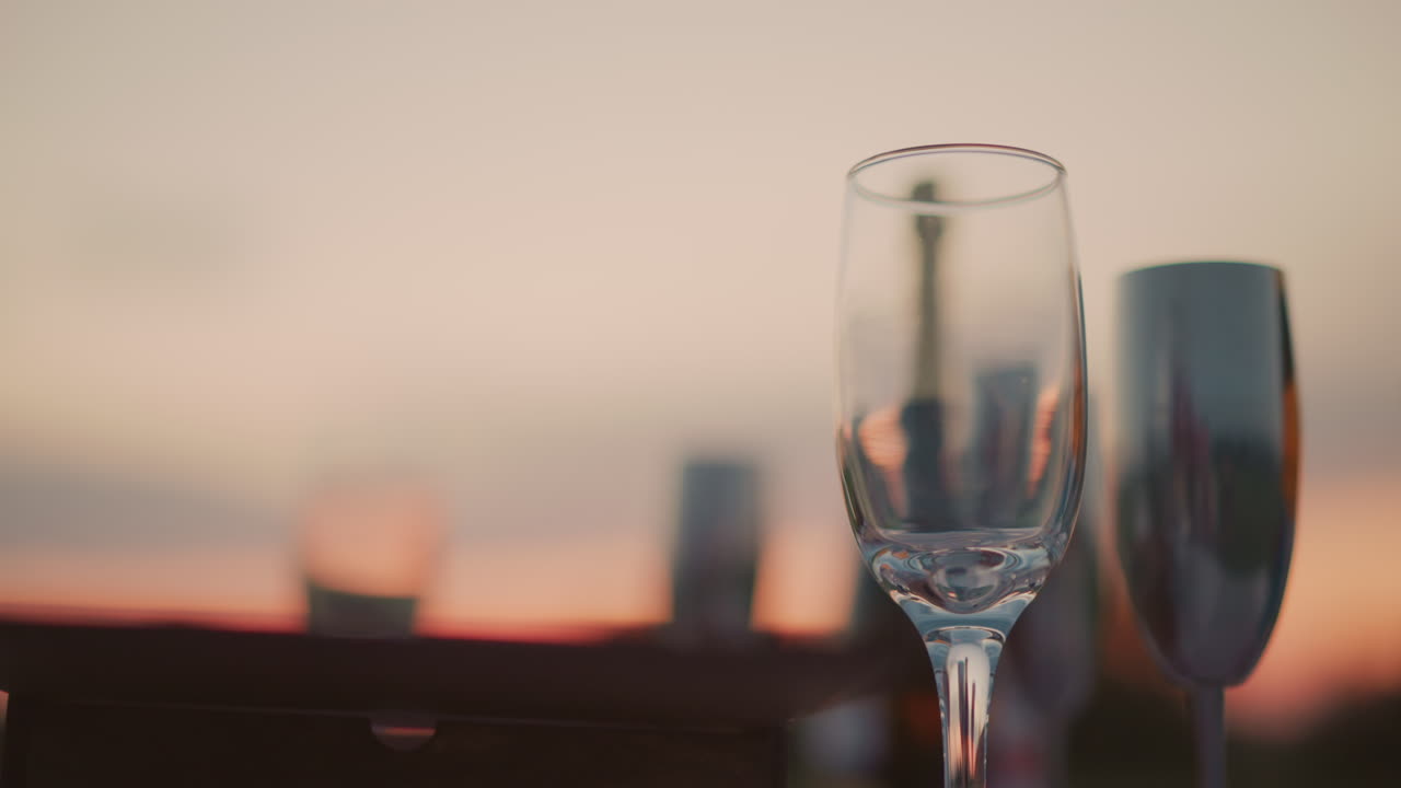 close up of empty wine glass on wooden surface at sunset with blurred bottles and landscape background reflecting warm light and soft colors capturing elegant beverage