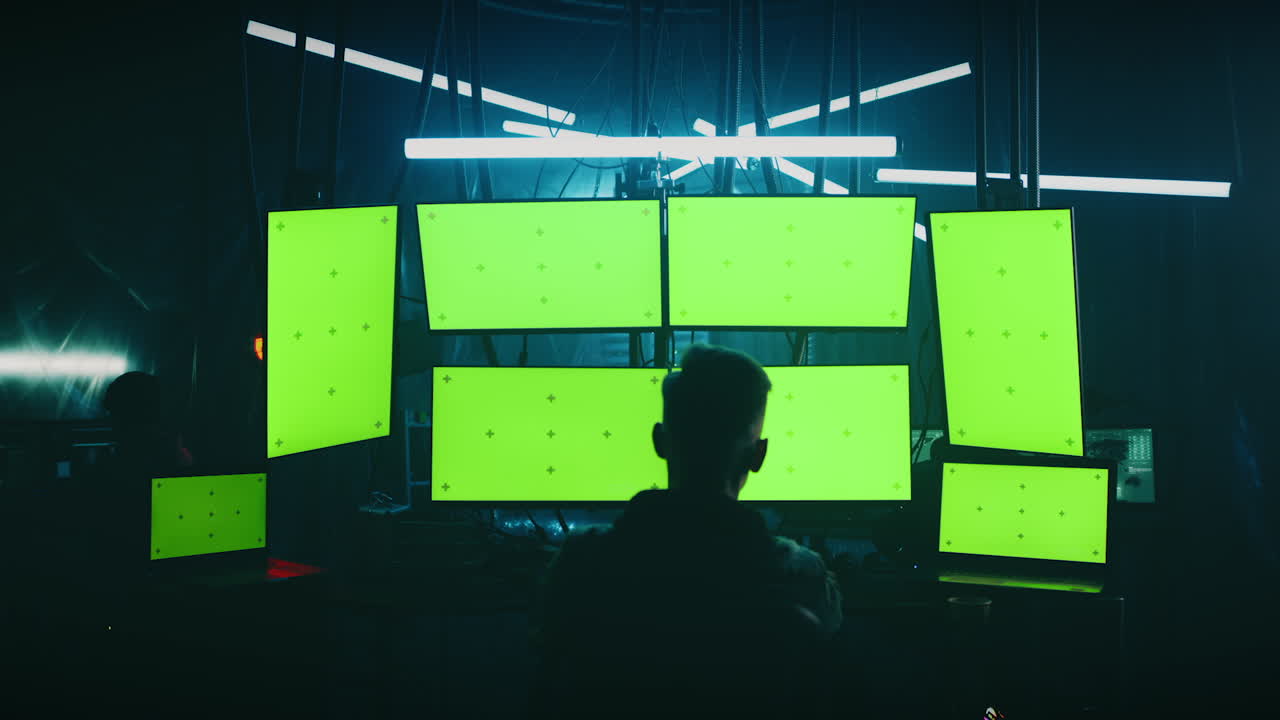Person Looking at Multiple Green Screen Monitors in a Dark Room