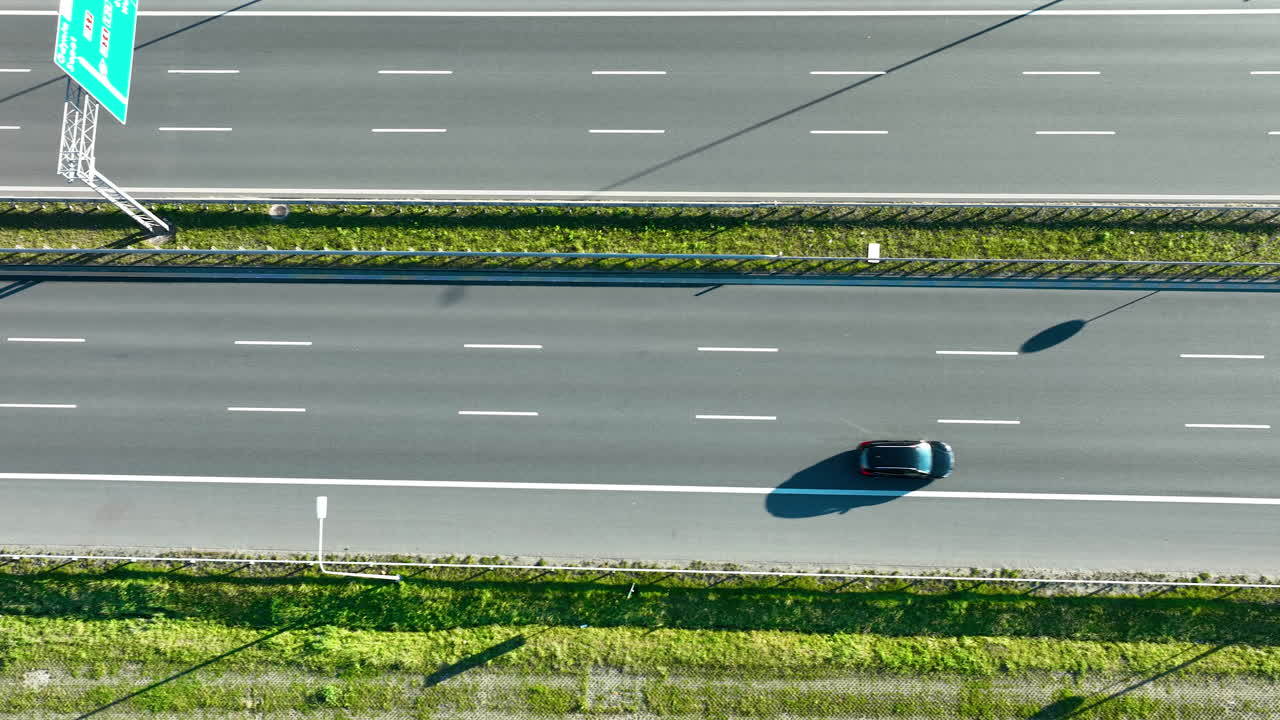 Aerial top‑down view of highway lanes with moving cars and a truck casting large shadows on sunny day