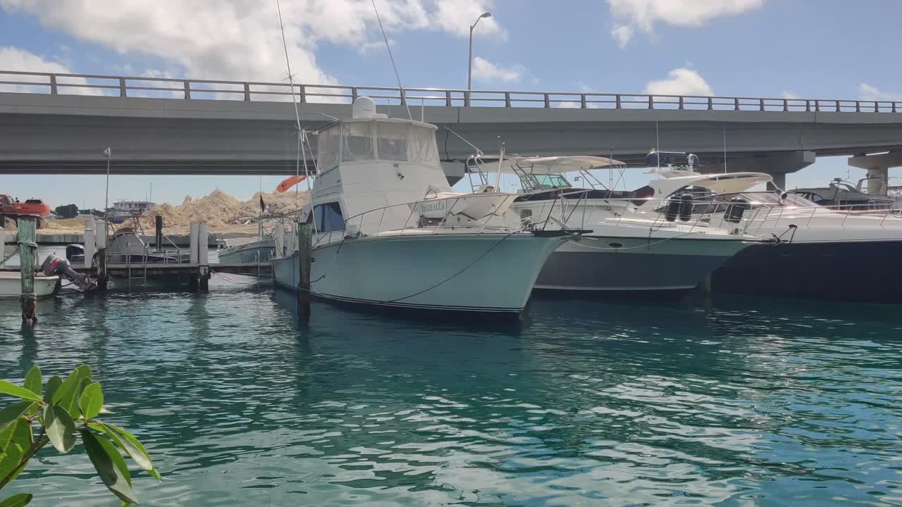 Moored luxury standfast yachts on a port near a bridge in the city of Nassau, Paradise Island in Bahamas. Pan right view in a clear sky day, 4K 30 FPS