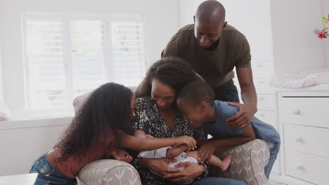 Liebevolle-Familie-Im-Kinderzimmer-Zu-Hause-Kuscheln-Ihren-Kleinen-Sohn,-Der-Im-Stuhl-Sitzt