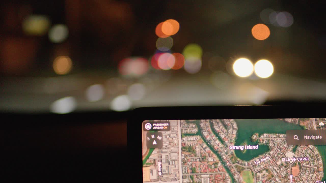 Driver navigates city streets at night using illuminated dashboard map and rear camera display
