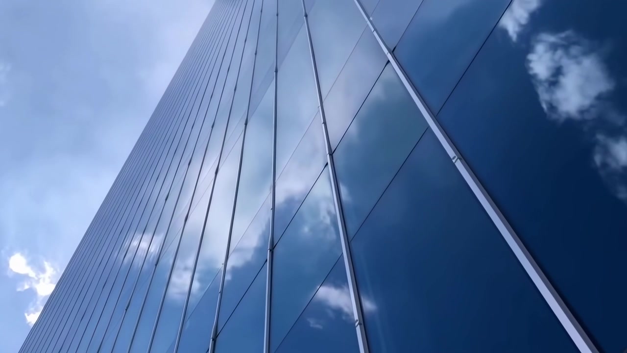Panorâmica para Cima de um Arranha-céu Moderno de Vidro Refletindo o Céu Azul e Nuvens