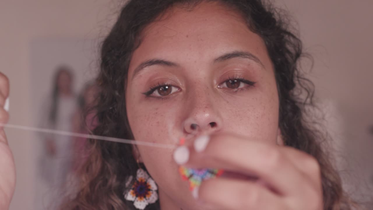 Closeup of woman&acute;s hands and brown eyes, making crafts with colorful little beads, needle and thread
